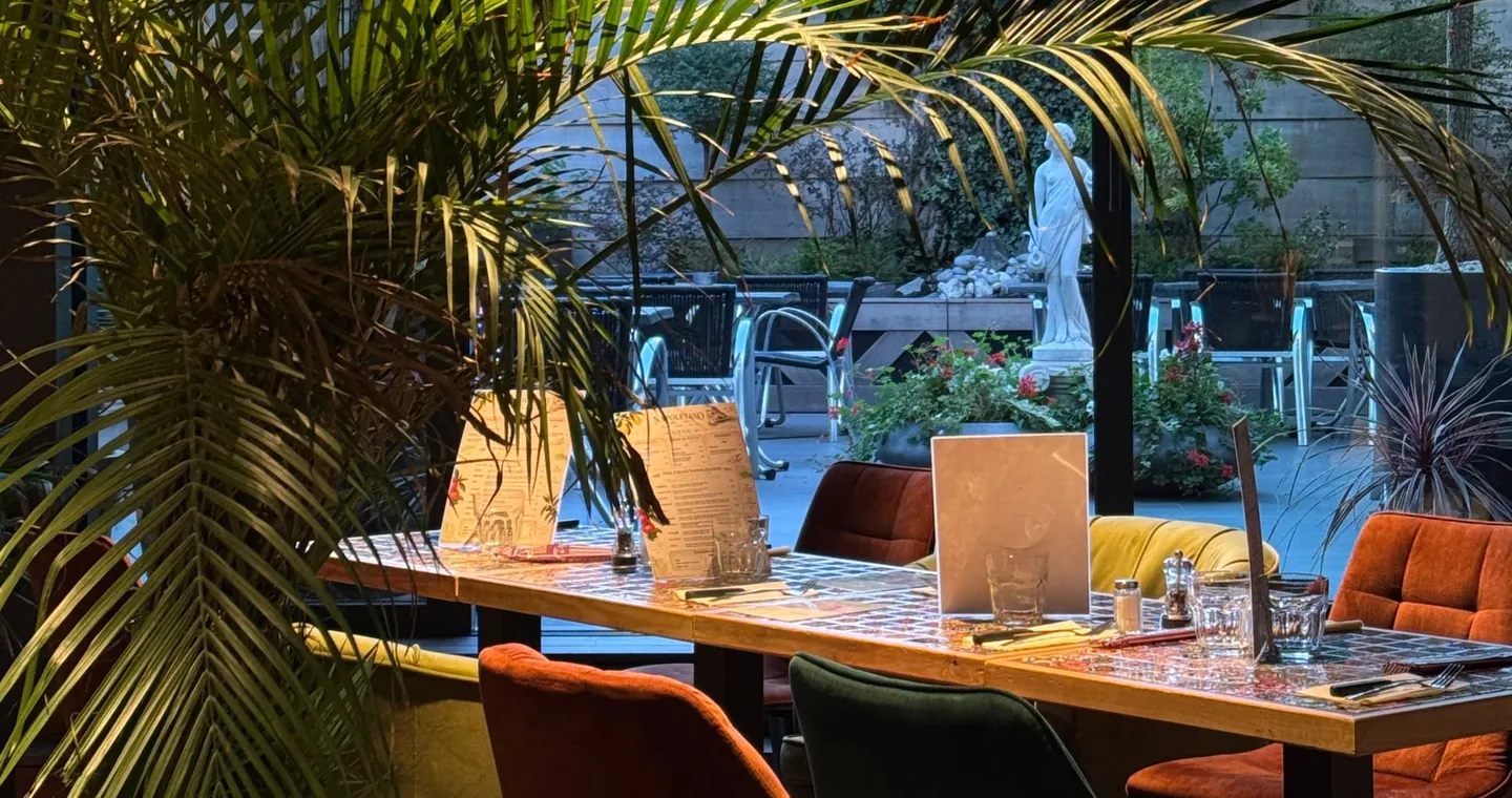 Inside Amore: emerald and rust velvet chairs, palm trees and wooden tables